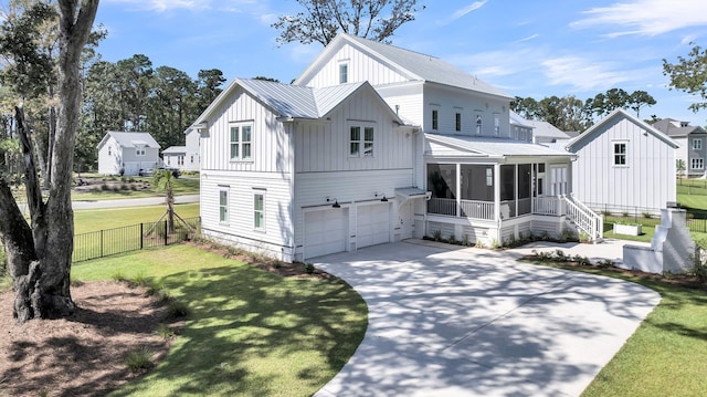 modern farmhouse featuring fence, a front yard, metal roof, a sunroom, and an attached garage