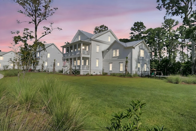 back of house at dusk featuring a lawn, board and batten siding, and a balcony