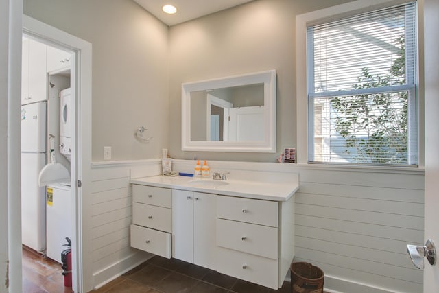 bathroom with wooden walls, stacked washer and dryer, wainscoting, tile patterned floors, and vanity