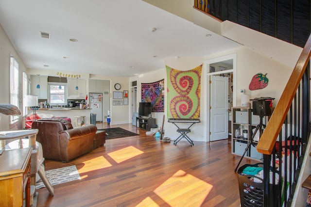 living area with stairs, wood finished floors, visible vents, and baseboards