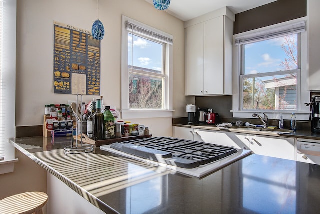 kitchen featuring gas cooktop, a sink, hanging light fixtures, white cabinetry, and dark countertops