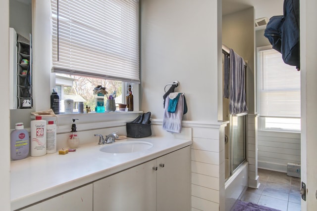 bathroom with a wealth of natural light, tile patterned flooring, wainscoting, and bath / shower combo with glass door