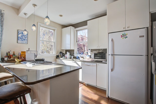 kitchen featuring white appliances, wood finished floors, white cabinets, pendant lighting, and a kitchen bar