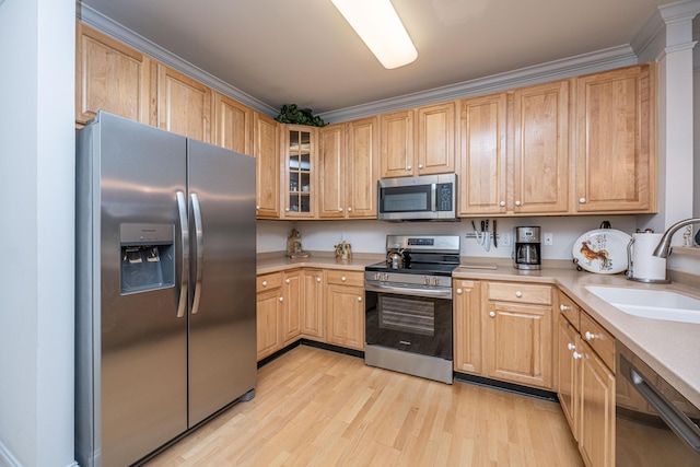 kitchen with light wood finished floors, light countertops, a sink, glass insert cabinets, and appliances with stainless steel finishes