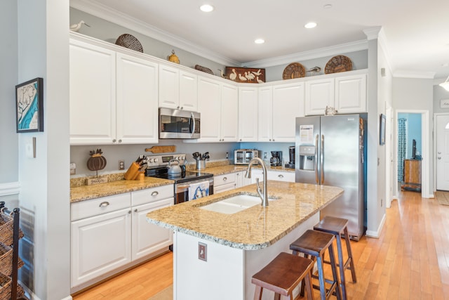 kitchen with ornamental molding, stainless steel appliances, sink, white cabinetry, and an island with sink