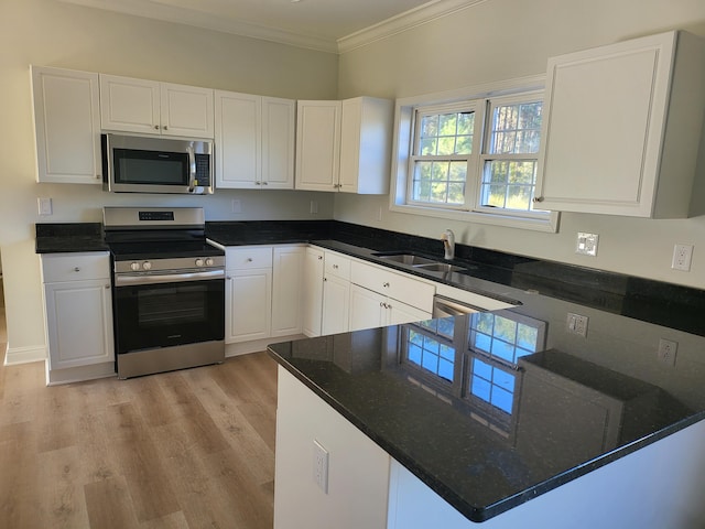 kitchen with appliances with stainless steel finishes, white cabinetry, dark stone counters, ornamental molding, and light hardwood / wood-style floors