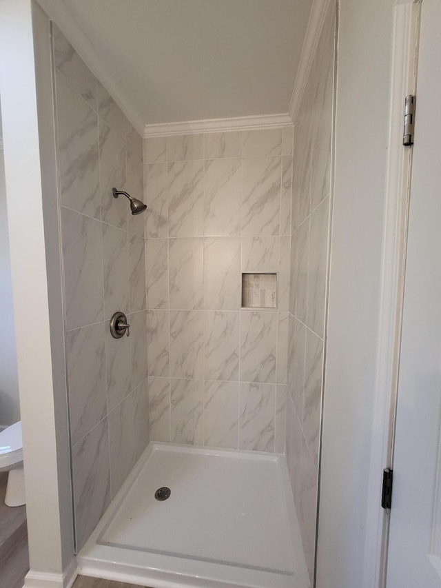 bathroom featuring toilet, crown molding, and tiled shower