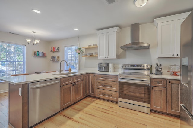 kitchen featuring wall chimney range hood, sink, hanging light fixtures, stainless steel appliances, and white cabinets