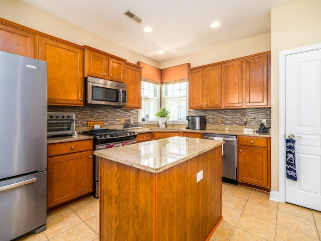 kitchen featuring visible vents, a sink, light stone counters, a center island, and stainless steel appliances