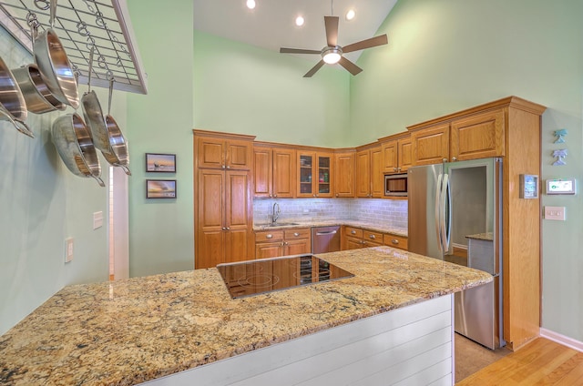13 32nd Ave, Isle Of Palms, SC 29451 - kitchen with stainless steel appliances, a high ceiling, a sink, brown cabinetry, and light stone counters