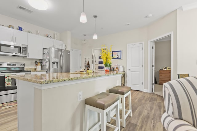 kitchen with visible vents, a kitchen breakfast bar, a center island with sink, light wood-style flooring, and stainless steel appliances