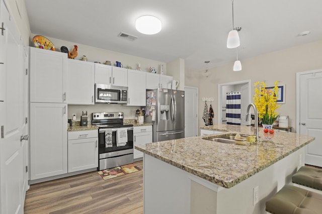 kitchen with hanging light fixtures, a sink, light wood-style flooring, stainless steel appliances, and visible vents