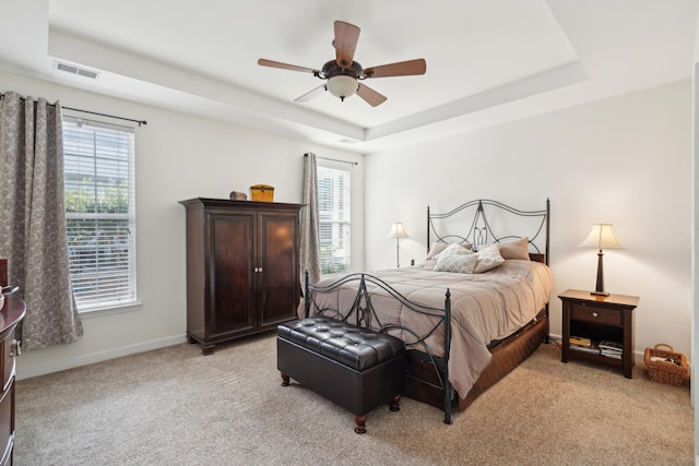 carpeted bedroom with a tray ceiling, multiple windows, and ceiling fan