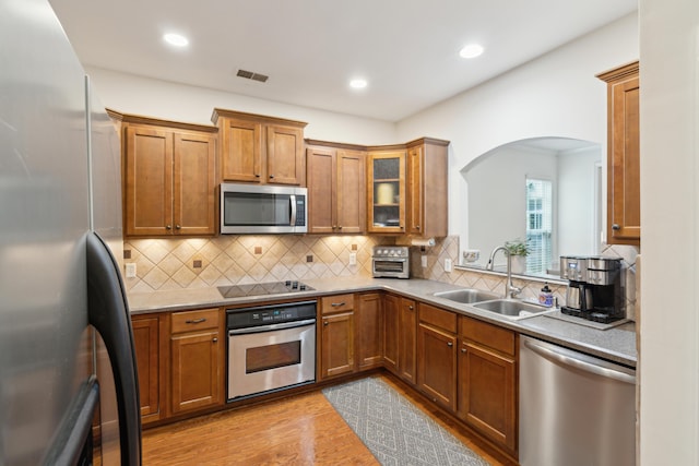 kitchen featuring light stone countertops, sink, stainless steel appliances, light hardwood / wood-style floors, and decorative backsplash