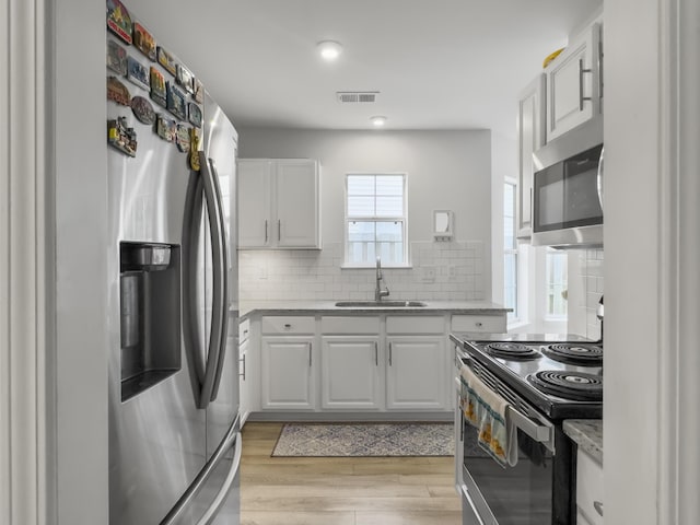 kitchen with stainless steel appliances, sink, white cabinets, and light hardwood / wood-style flooring