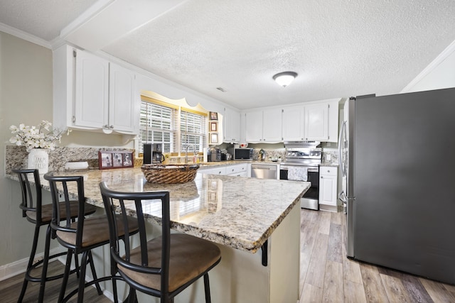 kitchen featuring kitchen peninsula, light stone countertops, a kitchen bar, white cabinetry, and stainless steel appliances