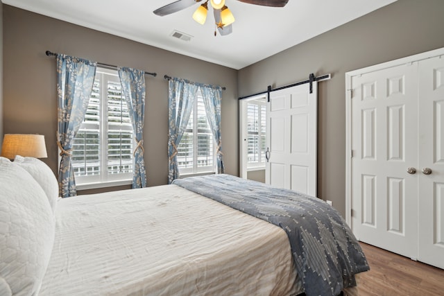 bedroom with wood-type flooring, ceiling fan, and a barn door