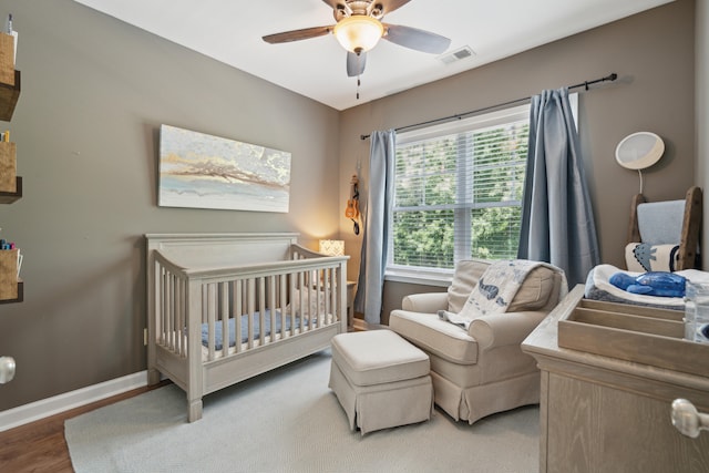 bedroom with hardwood / wood-style floors, ceiling fan, and a crib