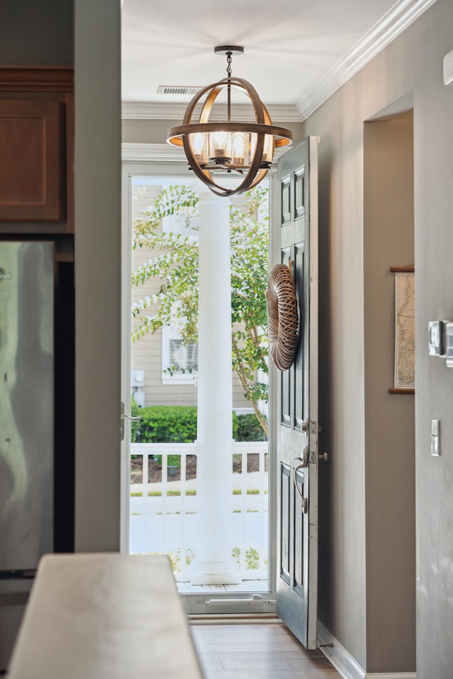 entryway featuring ornamental molding, light wood-type flooring, and a chandelier