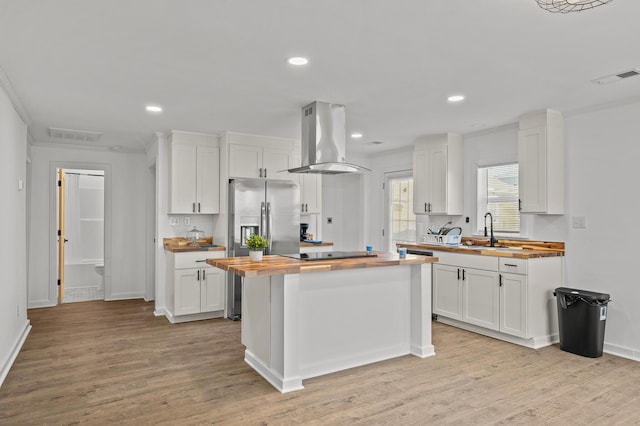 kitchen featuring visible vents, island exhaust hood, a sink, white cabinetry, and wooden counters