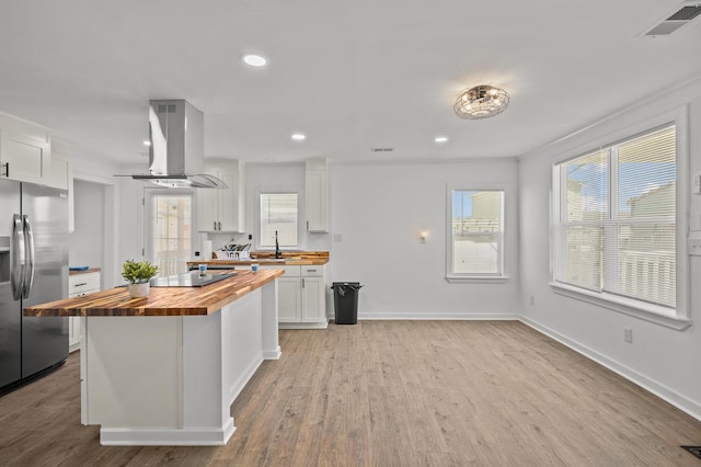 kitchen with butcher block counters, white cabinets, black electric stovetop, stainless steel fridge, and island range hood