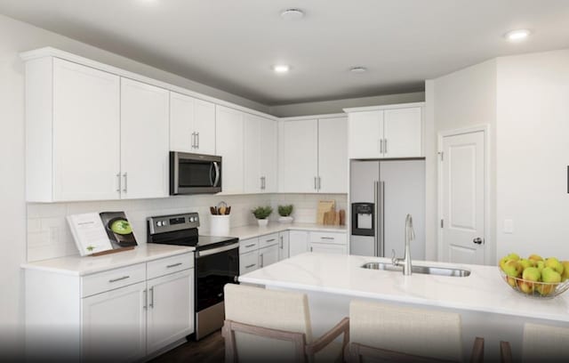 kitchen with white cabinets, sink, backsplash, stainless steel appliances, and a breakfast bar area