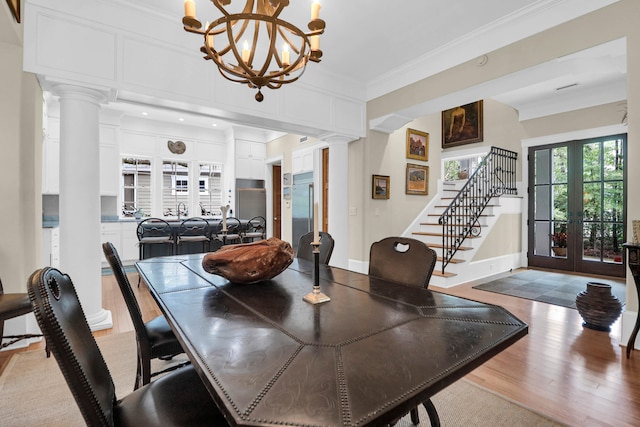 dining room with light hardwood / wood-style floors, ornate columns, crown molding, an inviting chandelier, and french doors