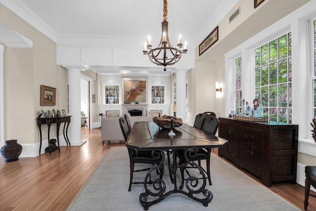 dining room with an inviting chandelier, decorative columns, hardwood / wood-style flooring, and crown molding