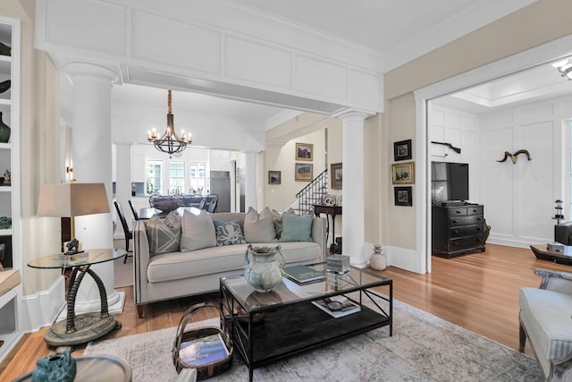 living room with a notable chandelier, hardwood / wood-style flooring, crown molding, and ornate columns