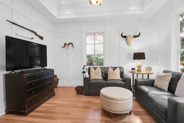 living room featuring light wood-type flooring, plenty of natural light, and a raised ceiling