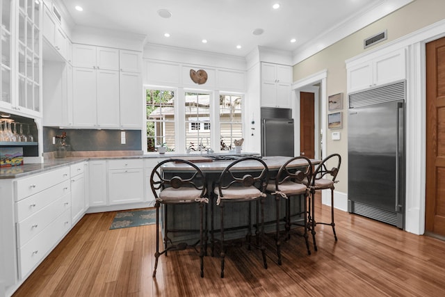 kitchen with stainless steel built in fridge, white cabinets, light wood-type flooring, and a kitchen island