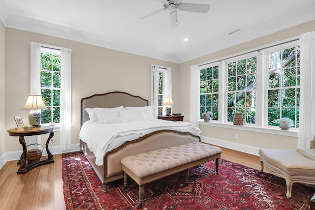 bedroom featuring multiple windows, wood-type flooring, ornamental molding, and ceiling fan