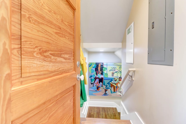 stairs featuring electric panel, lofted ceiling, and hardwood / wood-style flooring