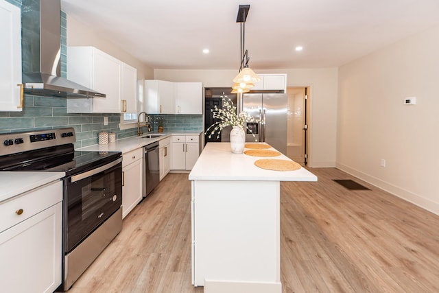 kitchen featuring white cabinetry, a kitchen island, wall chimney exhaust hood, stainless steel appliances, and light hardwood / wood-style flooring