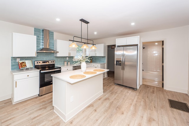 kitchen featuring pendant lighting, white cabinets, a kitchen island, wall chimney exhaust hood, and stainless steel appliances