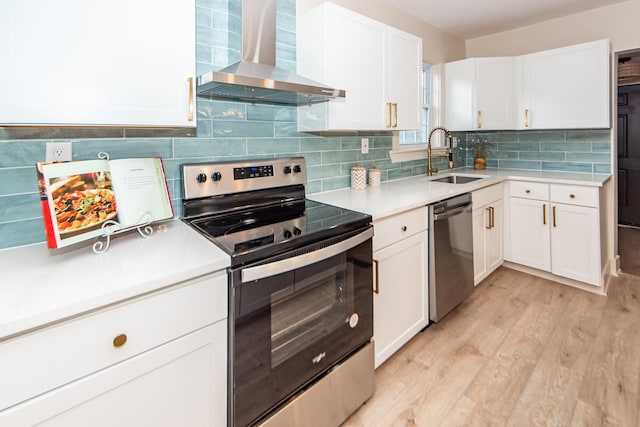 kitchen featuring wall chimney exhaust hood, white cabinetry, appliances with stainless steel finishes, and sink