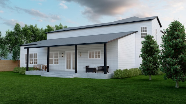 rear view of house with covered porch, a lawn, and fence