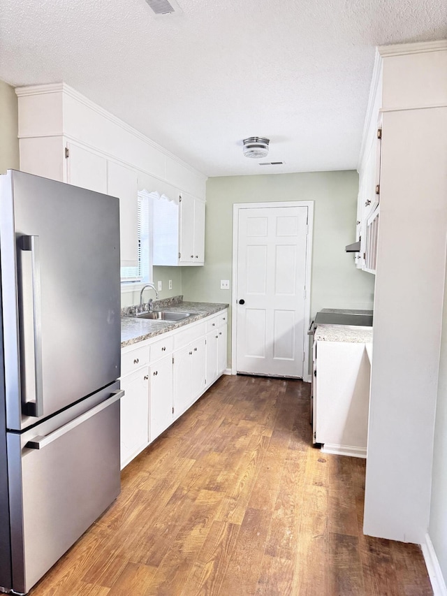 kitchen featuring sink, stainless steel refrigerator, white cabinetry, light wood-type flooring, and a textured ceiling