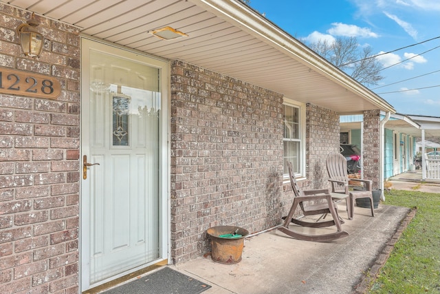 view of exterior entry with brick siding and a porch