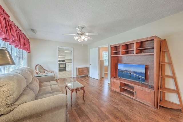 living area with a textured ceiling, visible vents, wood finished floors, and a ceiling fan