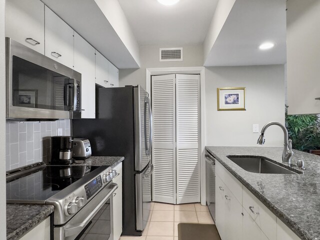 kitchen with dark stone counters, backsplash, white cabinetry, light tile patterned floors, and stainless steel appliances