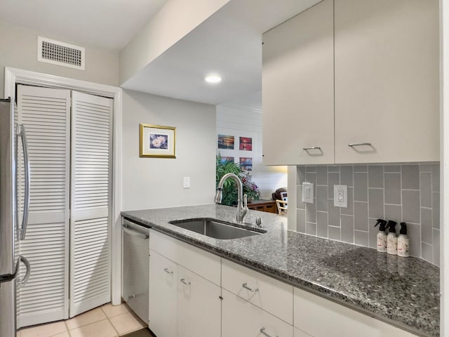 kitchen with dark stone counters, decorative backsplash, appliances with stainless steel finishes, light tile patterned floors, and sink