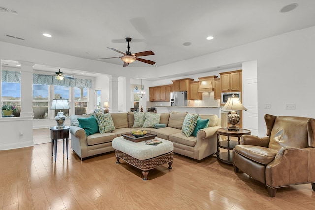 living room with ceiling fan with notable chandelier, light wood-type flooring, and ornate columns