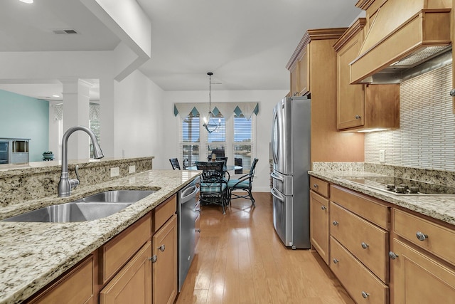 kitchen featuring sink, stainless steel appliances, light stone countertops, custom range hood, and decorative light fixtures