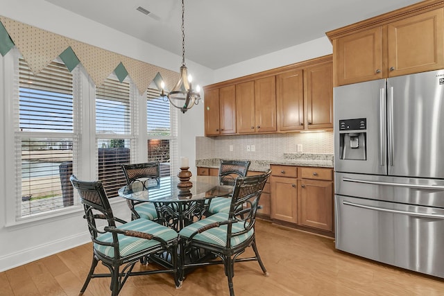 kitchen featuring light stone counters, stainless steel fridge, pendant lighting, light hardwood / wood-style floors, and backsplash