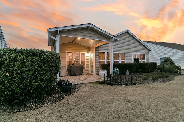 back house at dusk featuring a patio and a lawn