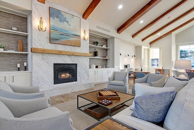 living room with beam ceiling, high vaulted ceiling, a fireplace, light hardwood / wood-style floors, and built in shelves