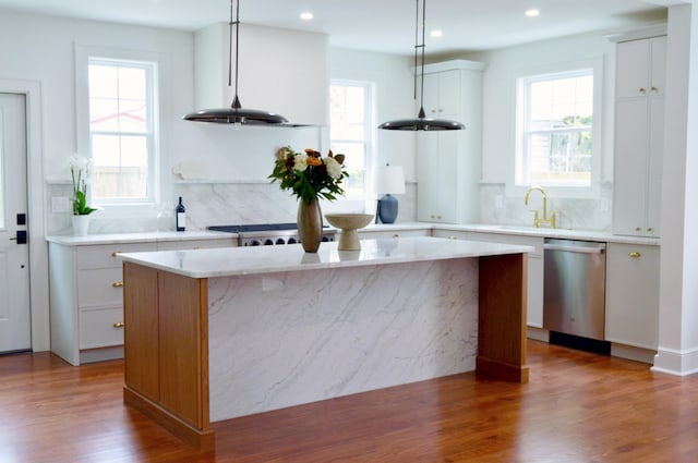 kitchen featuring a sink, a kitchen island, tasteful backsplash, wood finished floors, and stainless steel dishwasher