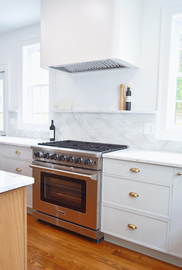 kitchen featuring custom range hood, light wood-style floors, light stone counters, white cabinets, and high end range