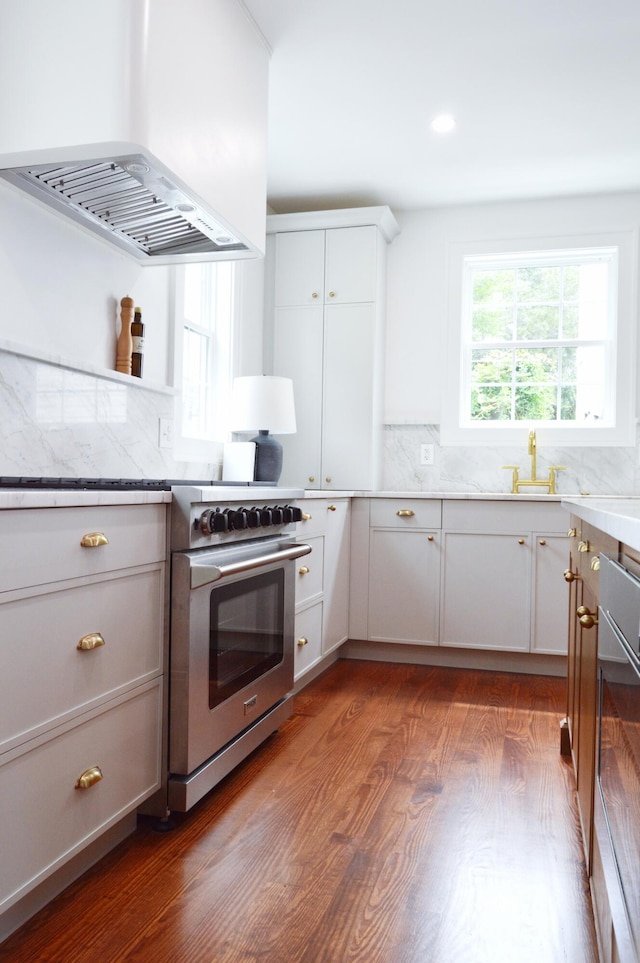 kitchen with decorative backsplash, high end range, wood finished floors, white cabinetry, and ventilation hood